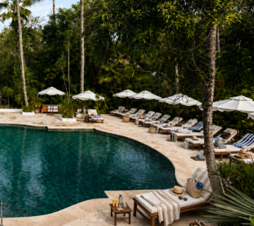 An empty tropical resort pool surrounded by sun loungers claimed with towels, hats, bags and bottles of sun cream 